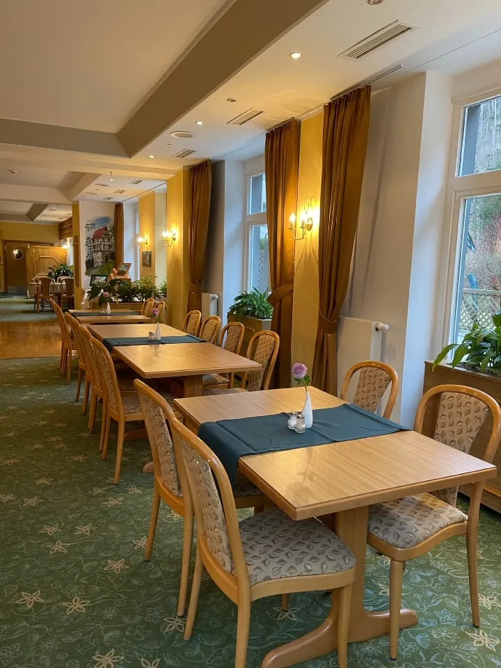 Restaurantbereich mit Holztischen und -stühlen, eingedeckt für Gäste, mit großen Fenstern.