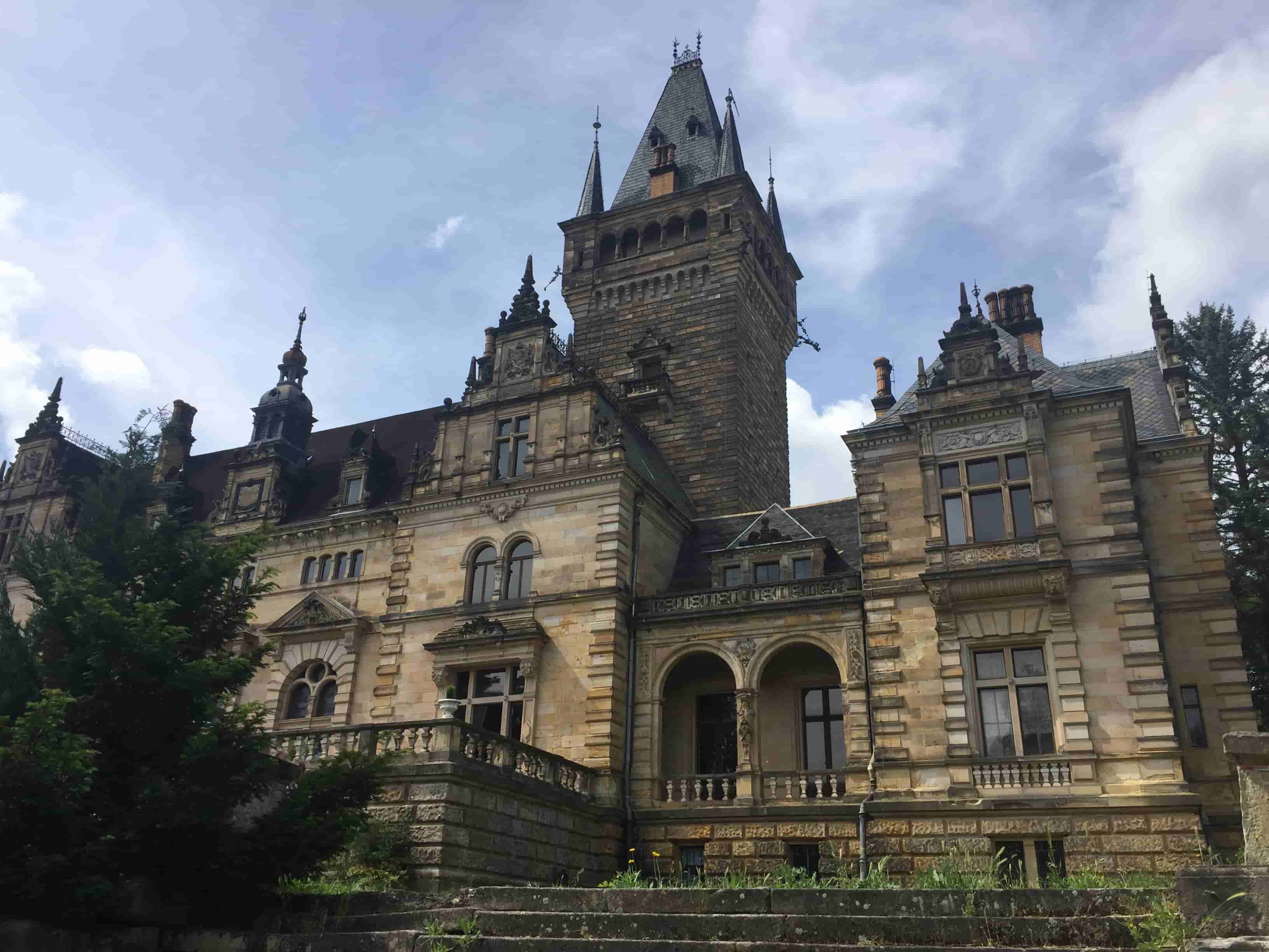 Historisches Schloss mit hohem Turm und verzierten Fassaden unter bewölktem Himmel.